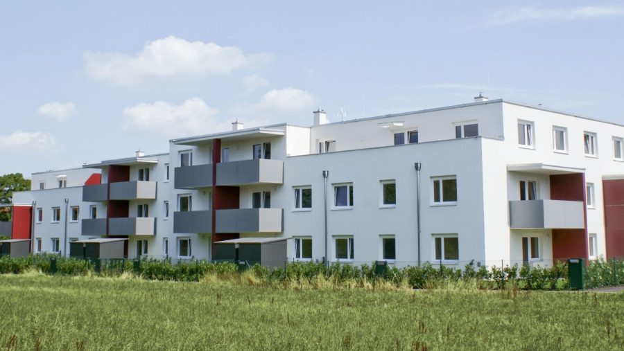Moderne Wohngebäude mit Balkonen auf freiem Feld unter blauem Himmel.