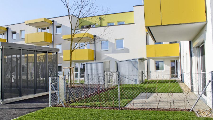 Mehrfamilienhaus mit gelben Balkonen und umzäunter Rasenfläche im modernen Design.