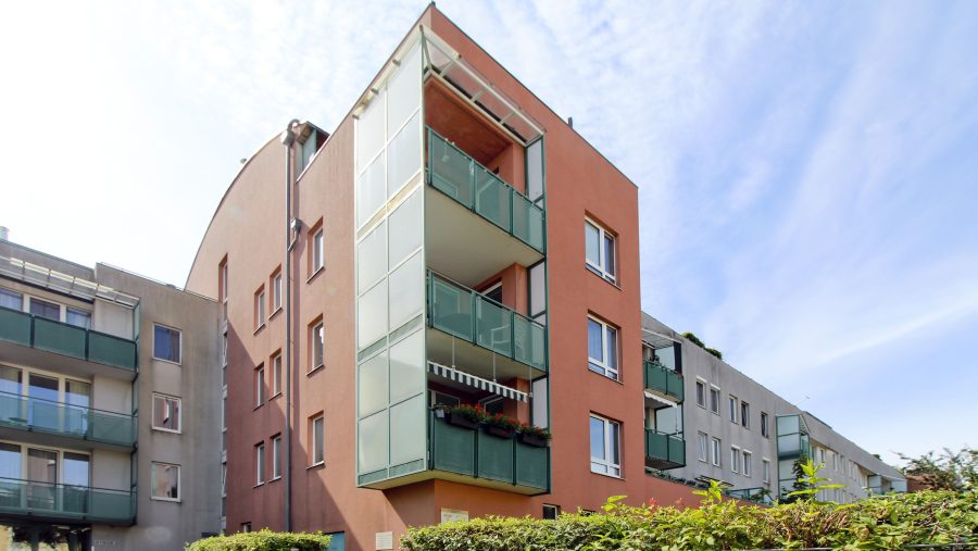 Moderne Wohngebäude mit Balkonen und roter Fassade unter blauem Himmel.