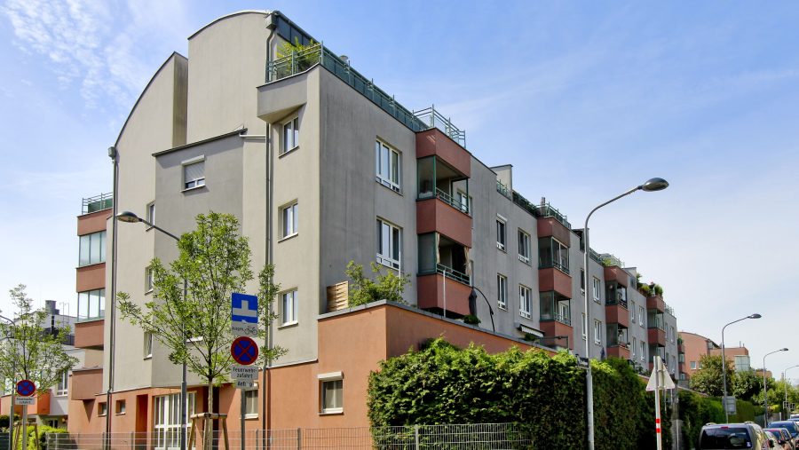 Modernes Wohngebäude an einer Straßenecke bei sonnigem Wetter in einer Stadt.