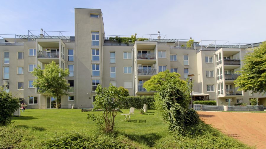 Mehrfamilienhaus mit modernen Balkonen und gepflegter Grünanlage im Vordergrund.