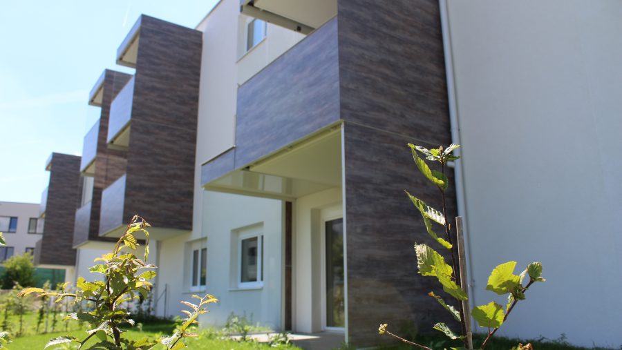 Moderne Wohngebäude mit Balkonen und Garten im Vordergrund bei sonnigem Wetter.