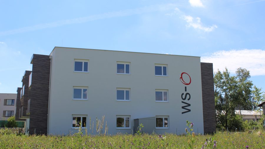 Modernes Mehrfamilienhaus mit Schriftzug, umgeben von Natur. Ideal für Wohnungskauf in ruhiger Lage.