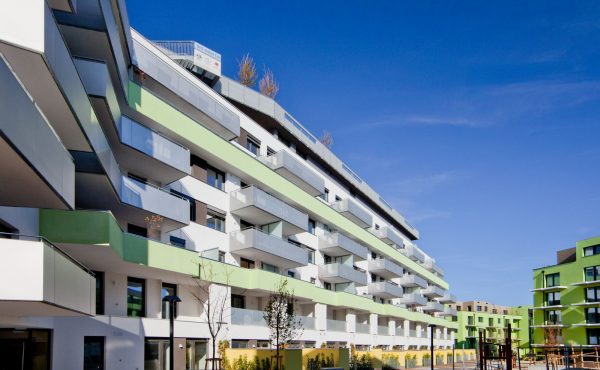 Moderne Wohngebäude mit Balkonen und einem Spielplatz im Vordergrund unter blauem Himmel.