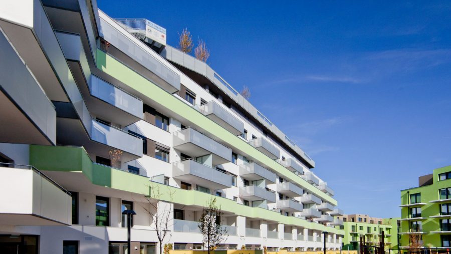 Moderne Wohngebäude mit Balkonen und einem Spielplatz im Vordergrund unter blauem Himmel.
