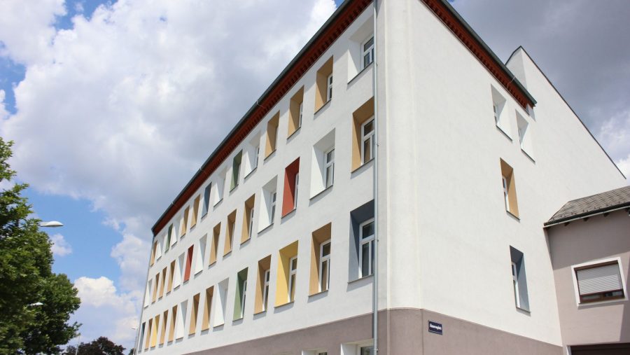 Mehrstöckiges Gebäude mit bunten Fensterrahmen an einem bewölkten Tag.