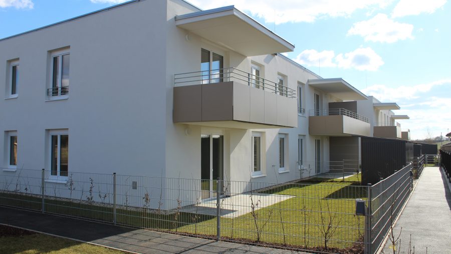 Moderne Wohngebäude mit Balkonen und Garten bei sonnigem Wetter.