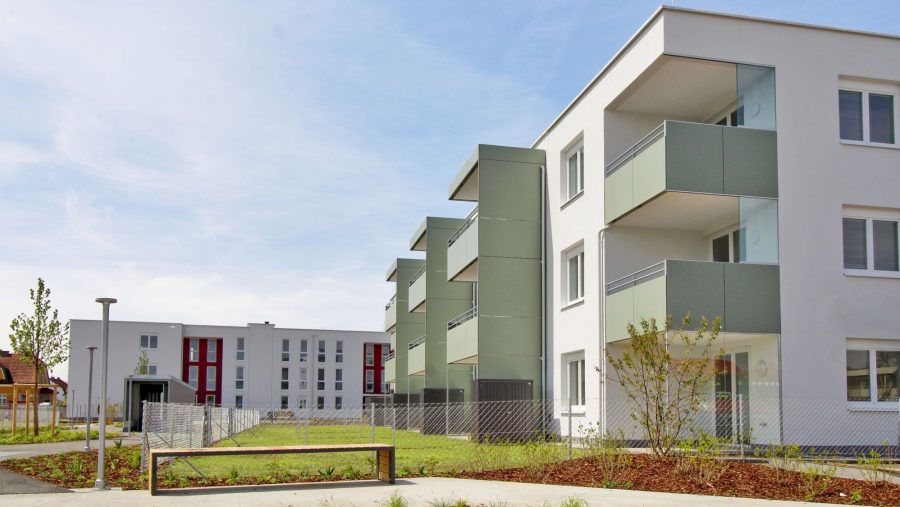 Mehrfamilienhäuser mit Balkonen und Gartenanlage an einem sonnigen Tag.