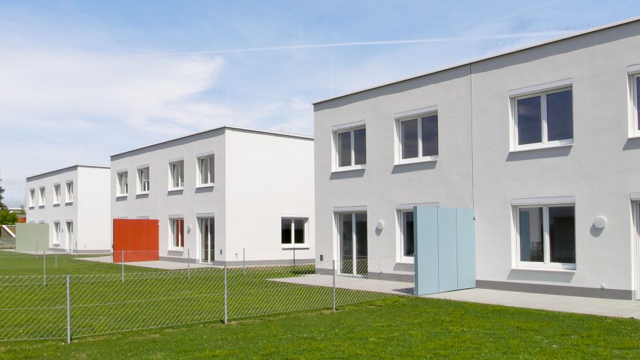 Moderne Reihenhäuser mit weißer Fassade und grünem Rasen bei sonnigem Himmel.