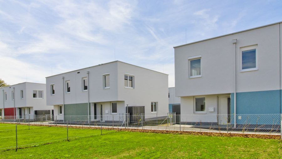 Moderne Reihenhäuser mit weißer Fassade und grünem Rasen bei sonnigem Wetter.