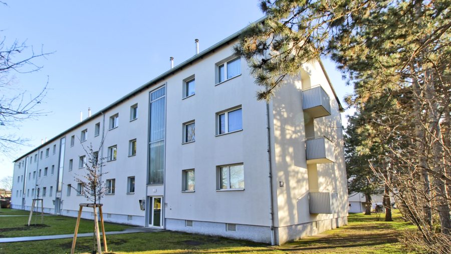 Mehrstöckiges Wohngebäude mit Balkonen und umgebender Grünfläche an einem sonnigen Tag.