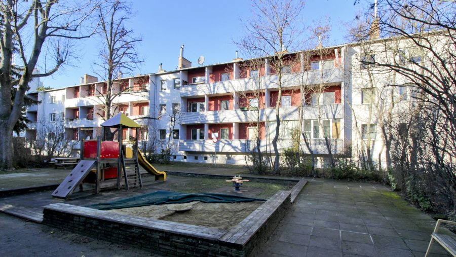 Mehrstöckiges Wohngebäude mit Spielplatz im Vordergrund bei sonnigem Wetter.