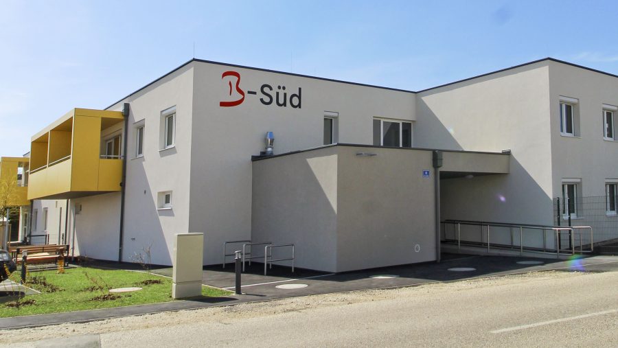 Modernes Bürogebäude mit gelbem Balkon und der Aufschrift B-Süd auf der Fassade bei Sonnenschein.