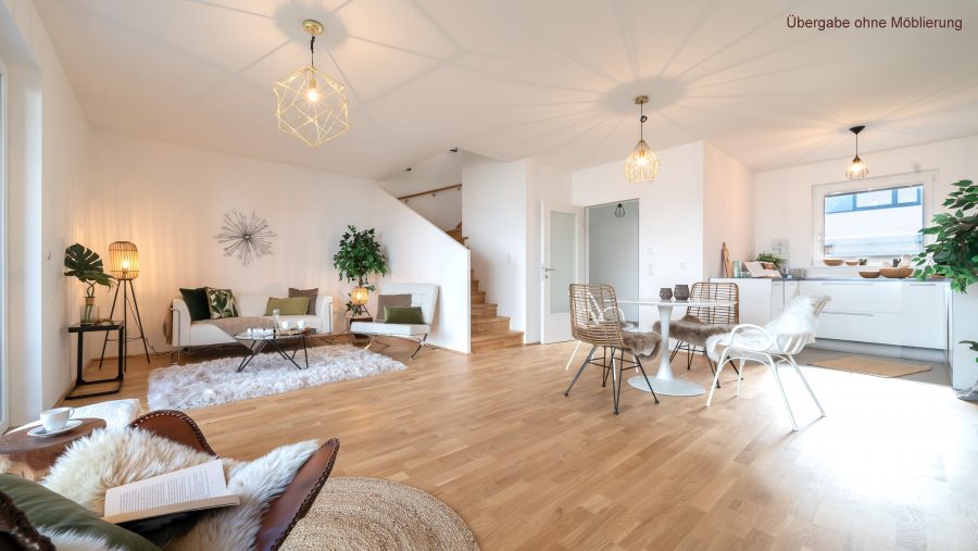 Helles, modernes Wohnzimmer mit offener Küche und Holzfußboden, gemütlich eingerichtet, Treppe im Hintergrund.