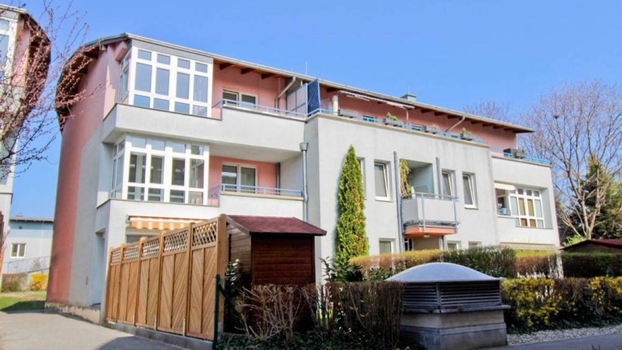 Mehrfamilienhaus mit Balkonen und Garten an einem sonnigen Tag.