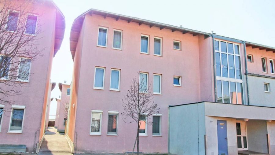 Mehrfamilienhaus mit rosa Fassade, blauer Himmel im Hintergrund.