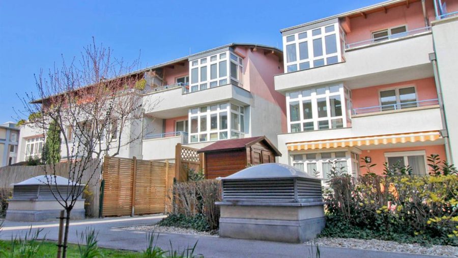 Mehrfamilienhaus mit modernen Balkonen und Gartenbereich bei sonnigem Wetter.