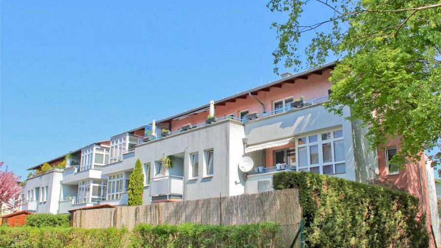 Mehrfamilienhaus mit Balkonen und Garten bei sonnigem Wetter.