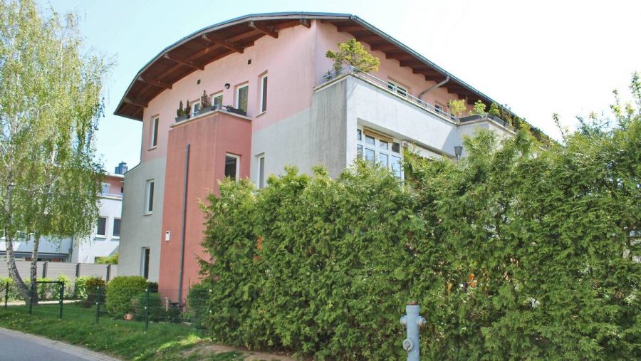 Modernes Wohngebäude mit bepflanztem Balkon und Garten in einer ruhigen Wohngegend, bei Sonnenschein.