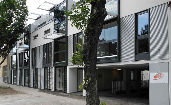 Moderne Gebäudeansicht mit großen Fenstern und Bäumen im Vordergrund.