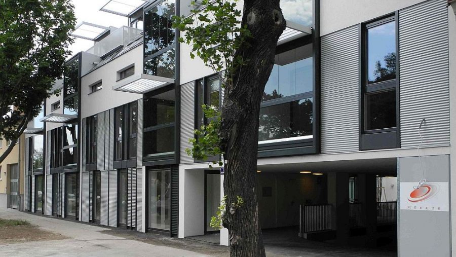 Moderne Gebäudeansicht mit großen Fenstern und Bäumen im Vordergrund.