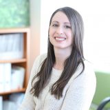 Lächelnde Frau in einem Büro, helle Einrichtung im Hintergrund.