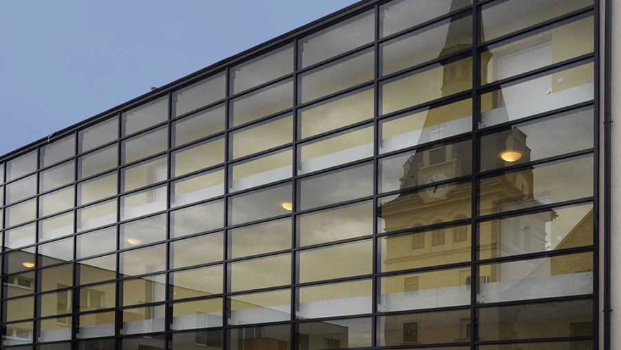 Spiegelung eines Kirchturms in einer modernen Glasfassade unter blauem Himmel.