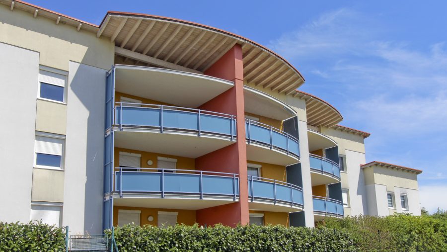 Moderne Wohngebäude mit Balkonen und blauer Fassade an einem sonnigen Tag.