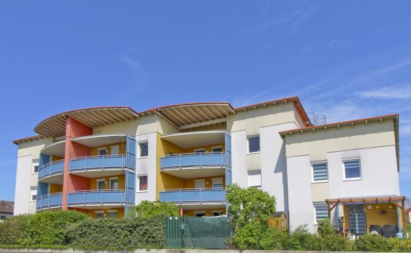 Mehrstöckiges modernes Wohngebäude mit Balkonen und blauer Fassade unter klarem Himmel.