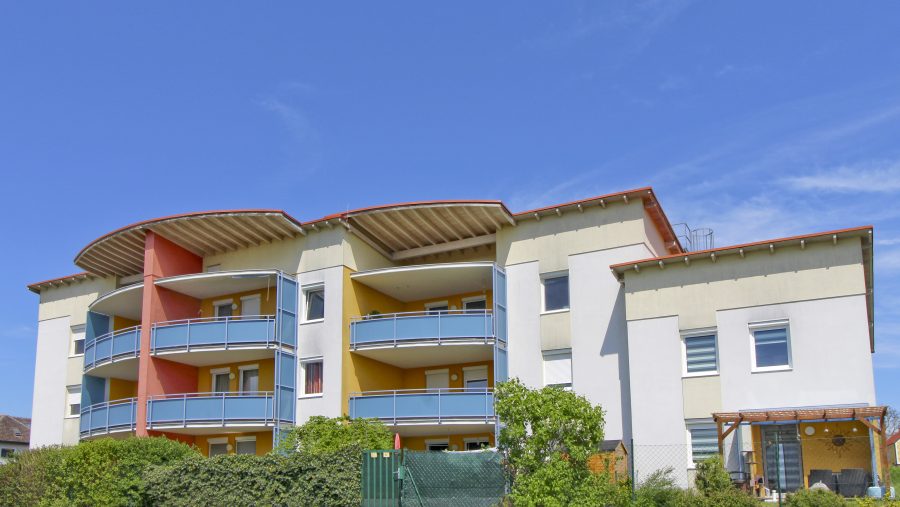 Mehrstöckiges modernes Wohngebäude mit Balkonen und blauer Fassade unter klarem Himmel.