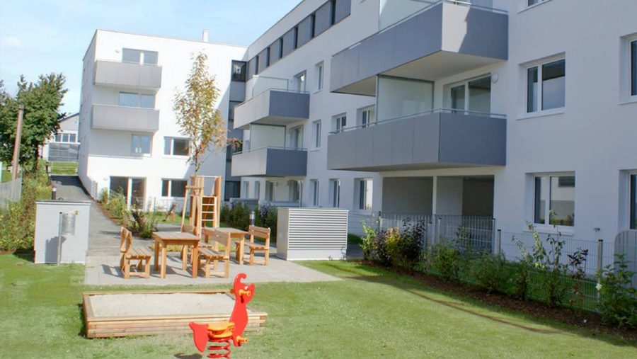 Moderne Wohnanlage mit Garten, Spielplatz und Balkonen an einem sonnigen Tag.