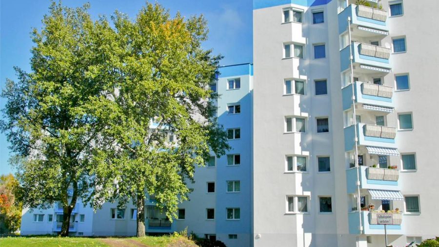 Mehrstöckiges Wohnhaus mit Balkonen und einem Baum im Vordergrund bei sonnigem Wetter.