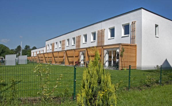 Moderne Reihenhäuser mit Terrasse und Garten im Grünen an einem sonnigen Tag.