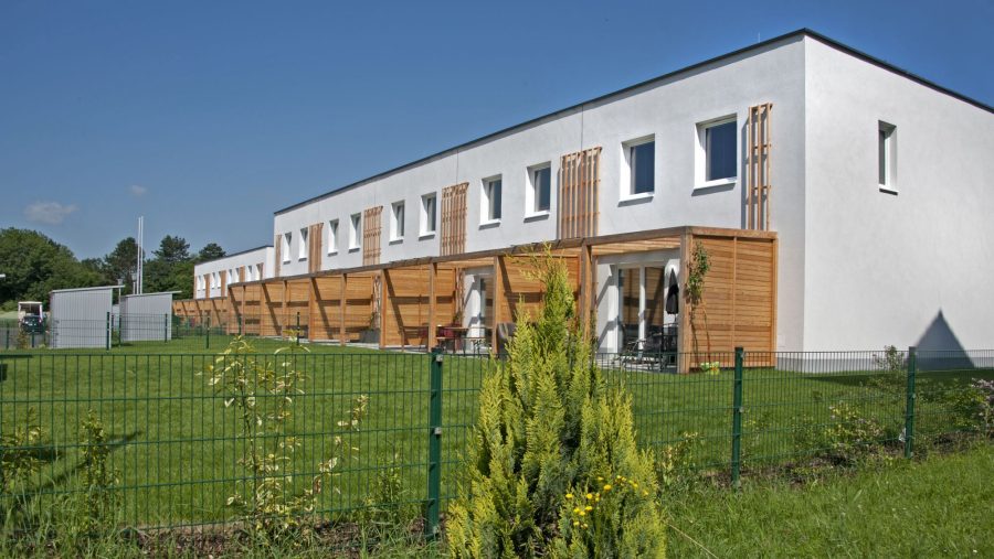 Moderne Reihenhäuser mit Terrasse und Garten im Grünen an einem sonnigen Tag.