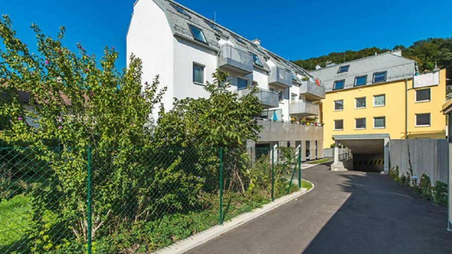 Moderne Wohngebäude mit Garten und Auffahrt an einem sonnigen Tag.