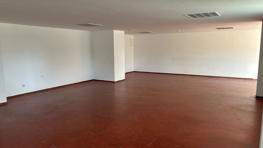 Leerer Raum mit weißen Wänden und rotem Boden, geeignet für Büro oder Lager.