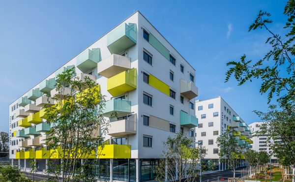 Moderne Wohngebäude mit bunten Balkonen vor blauem Himmel.