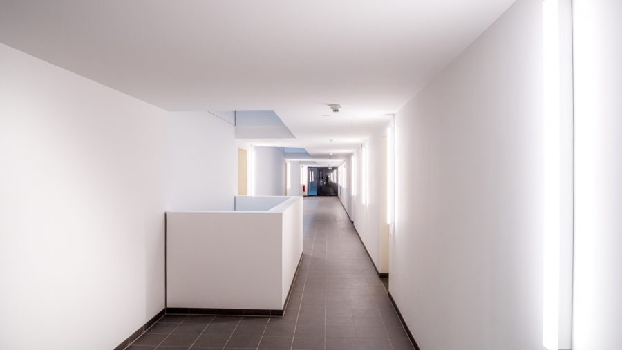 Moderner Flur mit hellen Wänden und Beleuchtung, die in die Ferne führt.