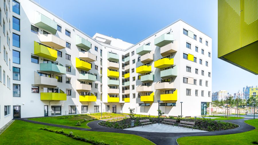 Moderne Wohnanlage mit gelben Balkonen und grüner Gartenanlage bei Tageslicht.