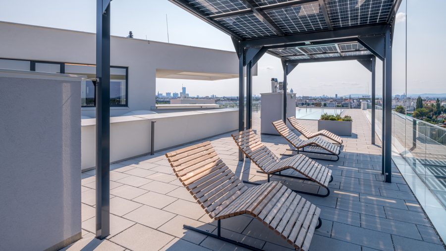 Dachterrasse mit Sonnenliegen und Blick auf die Stadt, überdacht mit Solarpanelen.