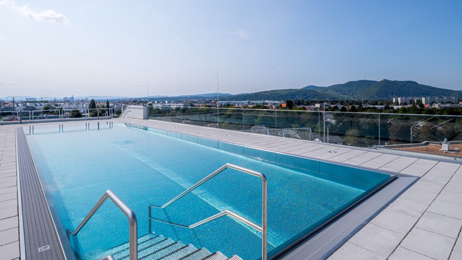 Rooftop-Pool mit Blick auf die Stadt und umliegende Berge an einem sonnigen Tag.