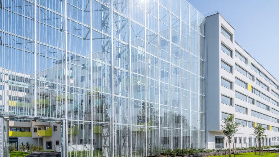 Moderner Bürokomplex mit Glasfassade und Garten bei sonnigem Wetter.