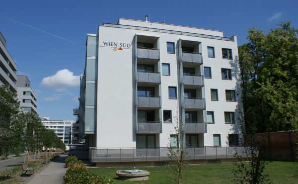 Moderne Wohngebäude mit Balkonen und grünem Vorplatz unter blauem Himmel.