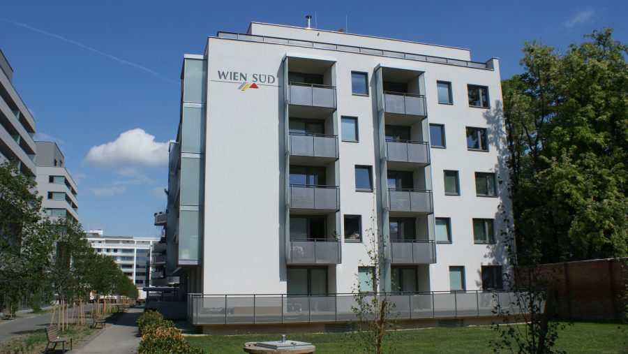 Moderne Wohngebäude mit Balkonen und grünem Vorplatz unter blauem Himmel.