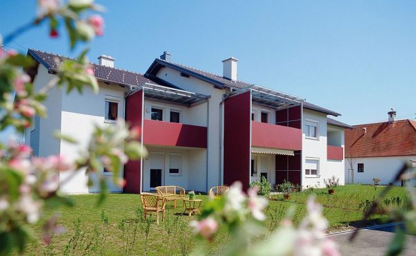 Zweistöckiges weiß-rotes Wohnhaus mit Garten im Frühling, blauer Himmel.