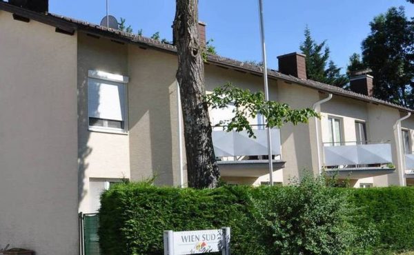 Wohnhaus mit Garten, Sommer, blauer Himmel, moderne Architektur, Bäume im Hintergrund.