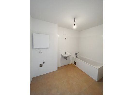 Leeres Badezimmer mit Badewanne, Waschbecken und beigen Fliesen. Weiße Wände und Decke mit einfacher Beleuchtung.