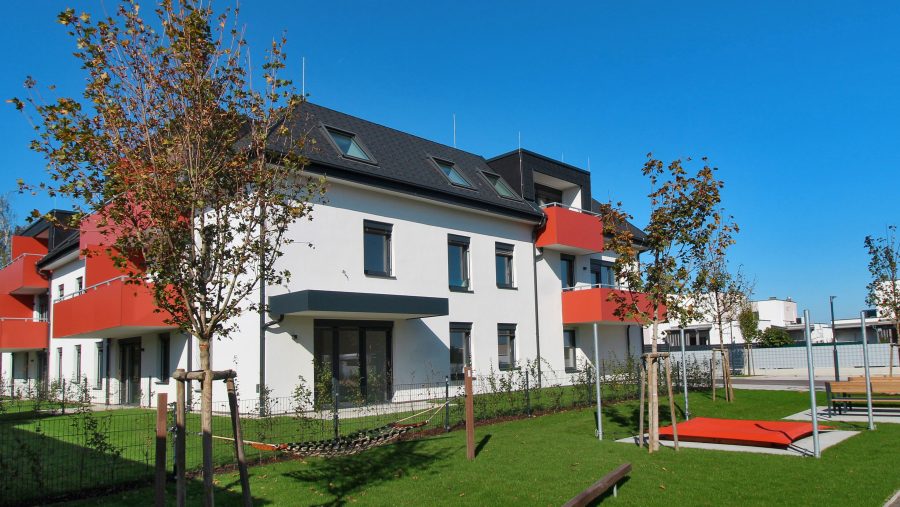 Moderne Wohnanlage mit Balkonen und gepflegtem Garten bei klarem Himmel.