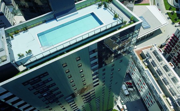 Hochhaus mit Dachterrasse und Pool, umgeben von moderner Stadtarchitektur.