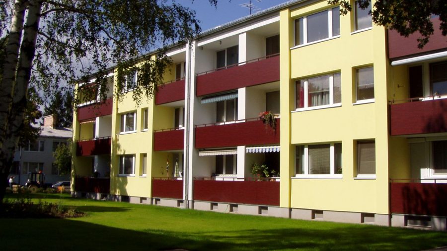 Gelbes Wohnhaus mit Balkonen und grünem Rasen im Vordergrund an einem sonnigen Tag.